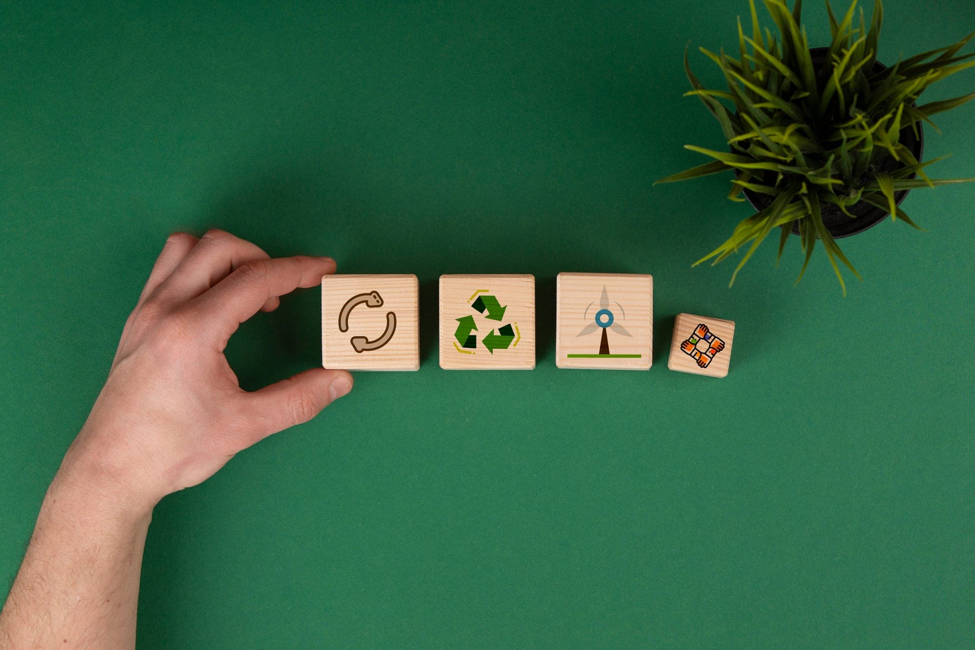 A hand arranging wooden blocks printed with recycling and renewable-energy symbols.