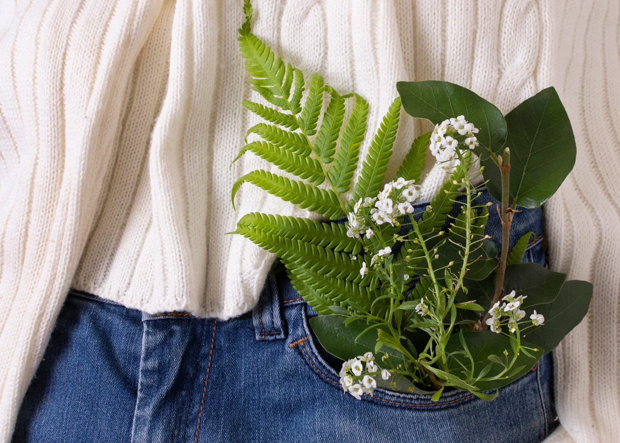 A cream knitted sweater over denim with fern and blossom in the pocket.