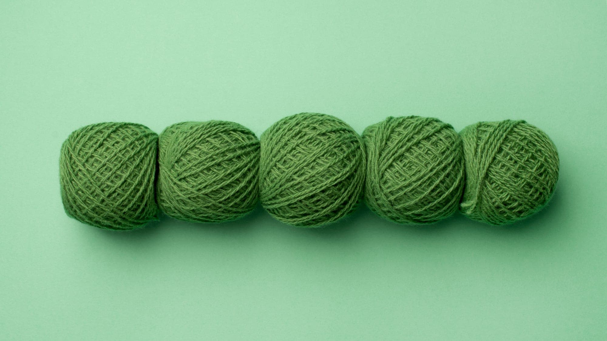 Five balls of green wool yarn in a row.