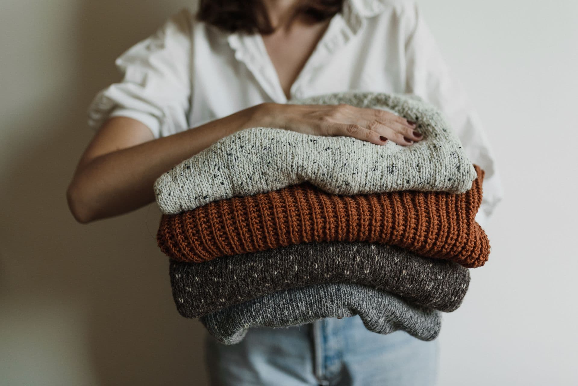 Folded knitted sweaters carried in both arms.