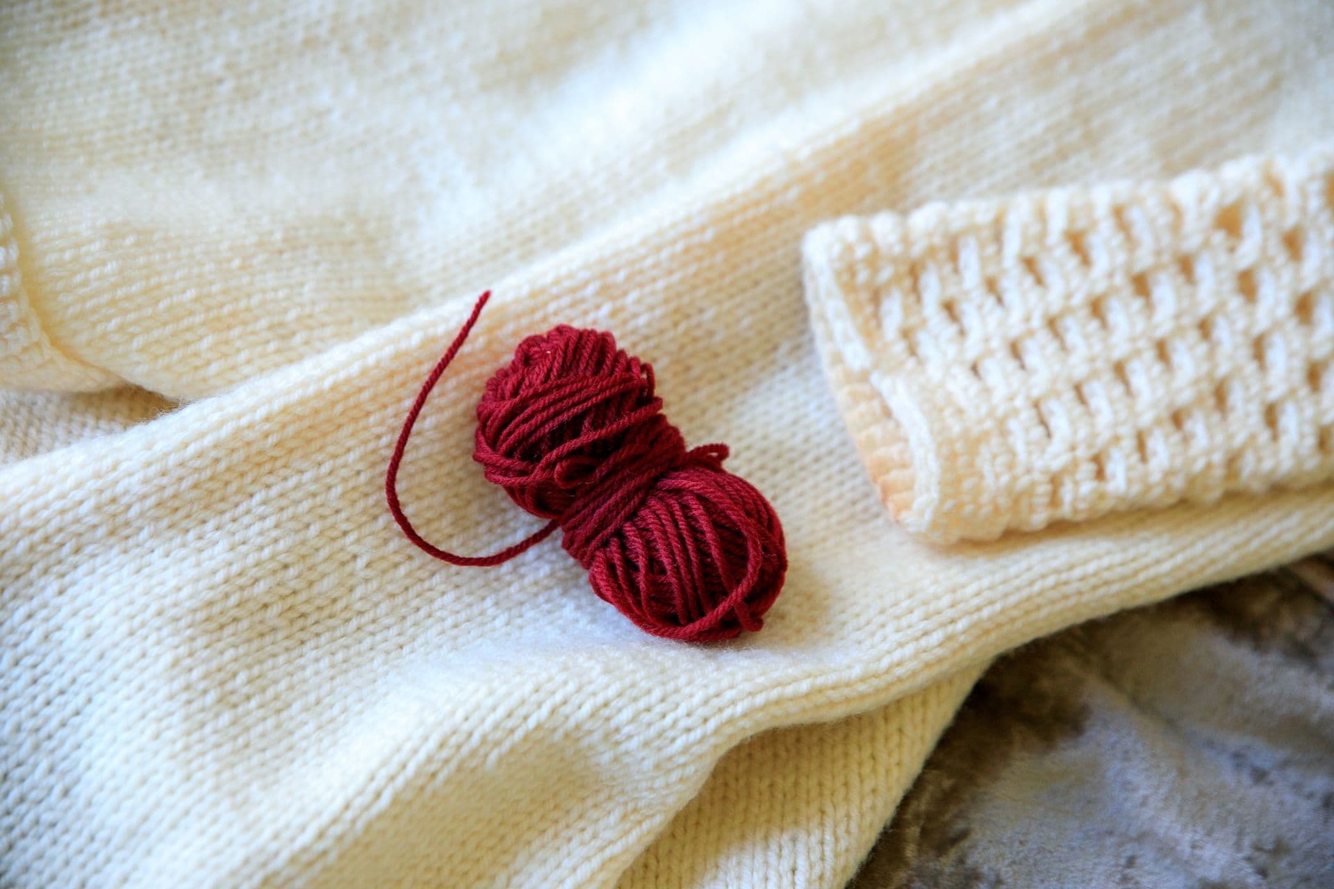 A knitted swatch and a ball of yarn on a cream sweater.