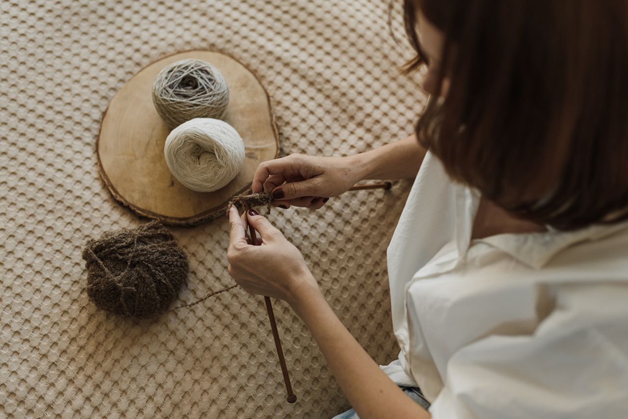 Hands knitting a swatch beside balls of undyed wool.